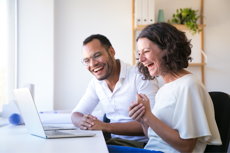 man and woman sitting in front of laptop smiling broadly