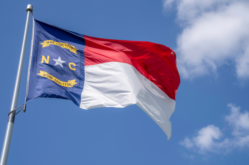 north carolina state flag on flag pole against blue sky